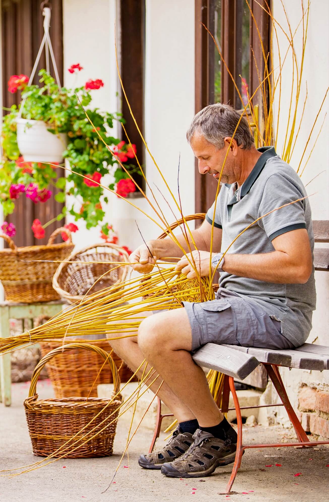 Der Hausherr sitzt auf einer Holzbank und flechtet Weidenkörbe.