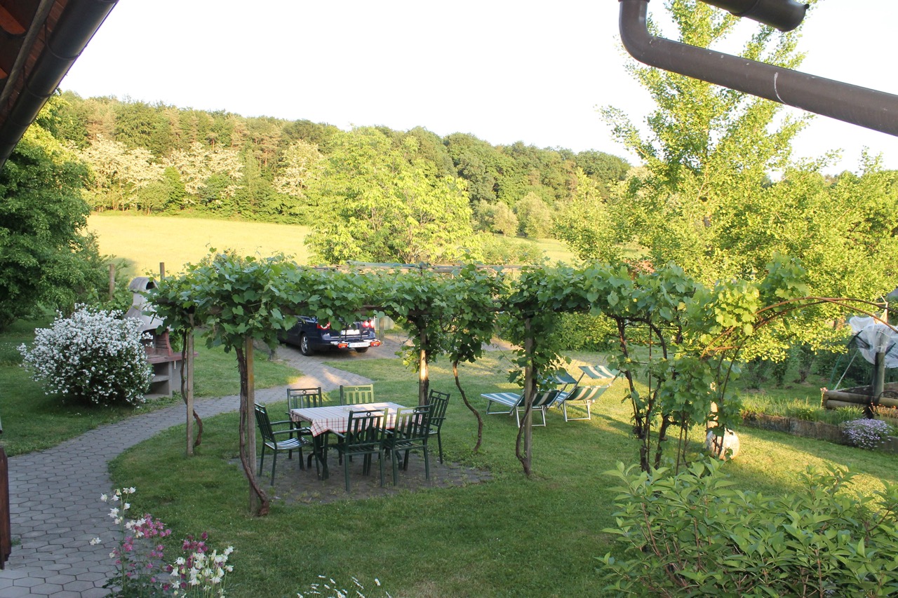 Schöner Garten mit Weinlaube und Sitzgelegenheit. Man sieht auch gemütliche Liegestühle. Panoramabllick bis zum angrenzenden Waldrand