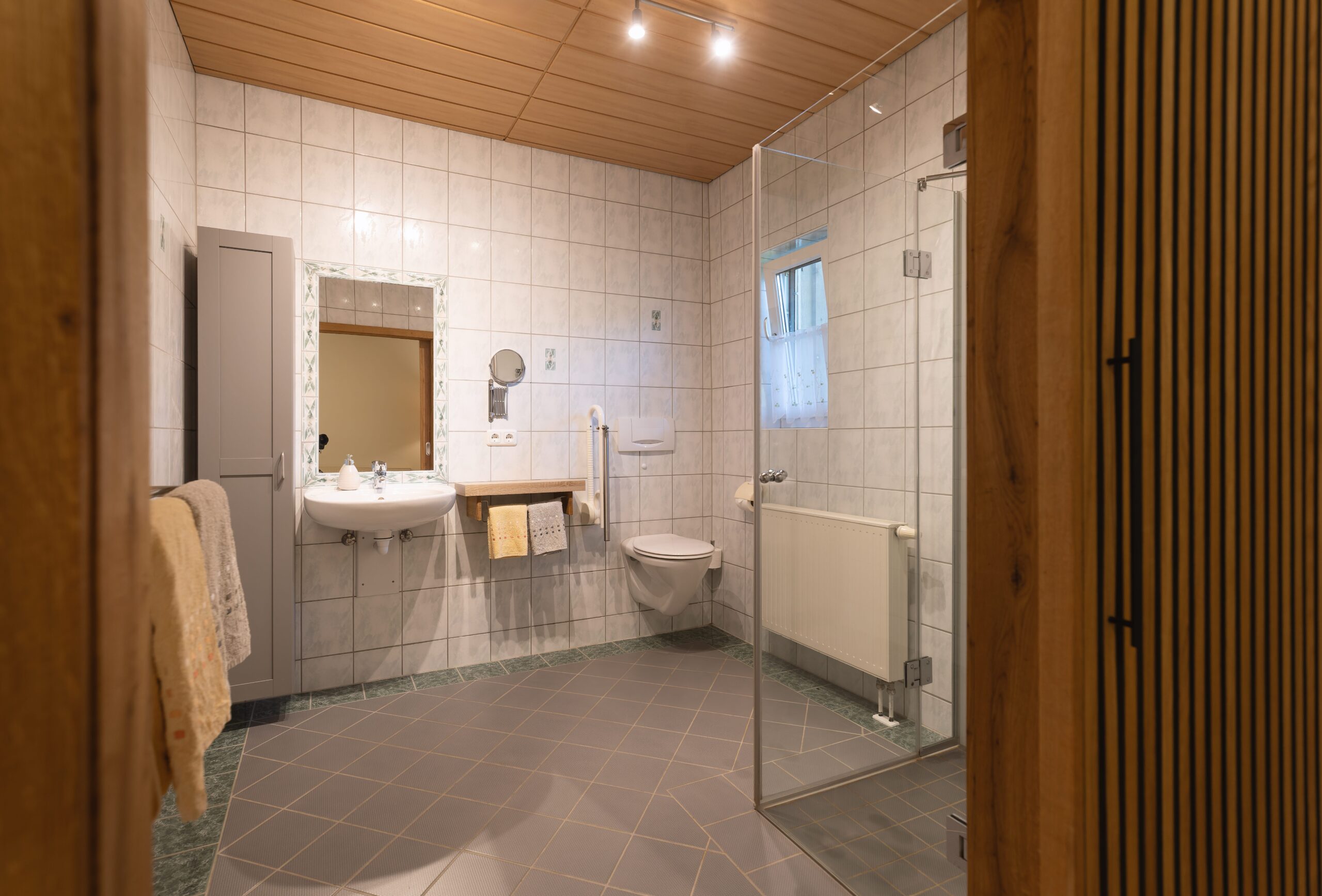 Großes barrierefreies Badezimmer mit Fenster, Dusche und WC mit Haltegriffe. Unterfahrbares Waschbecken. Rutschfeste Fliesen.