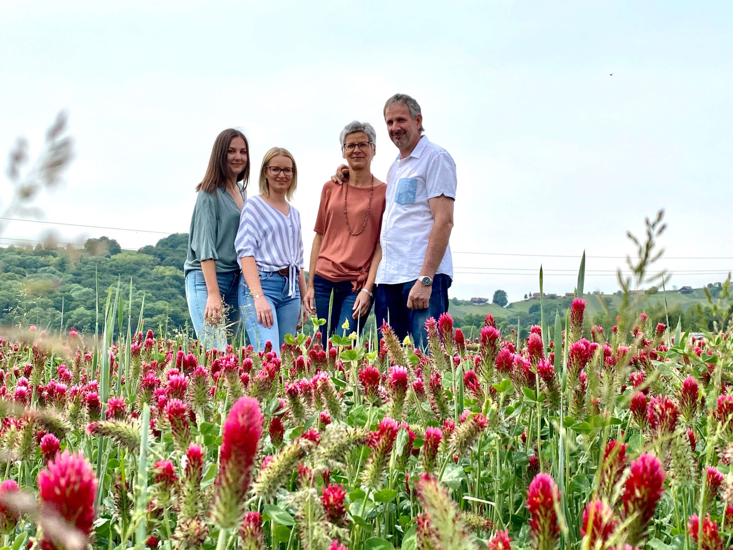 Silvia, Alexander mit den beiden Töchtern stehen in der roten Blumenwiese. Dahinter ein schönes Panorama.