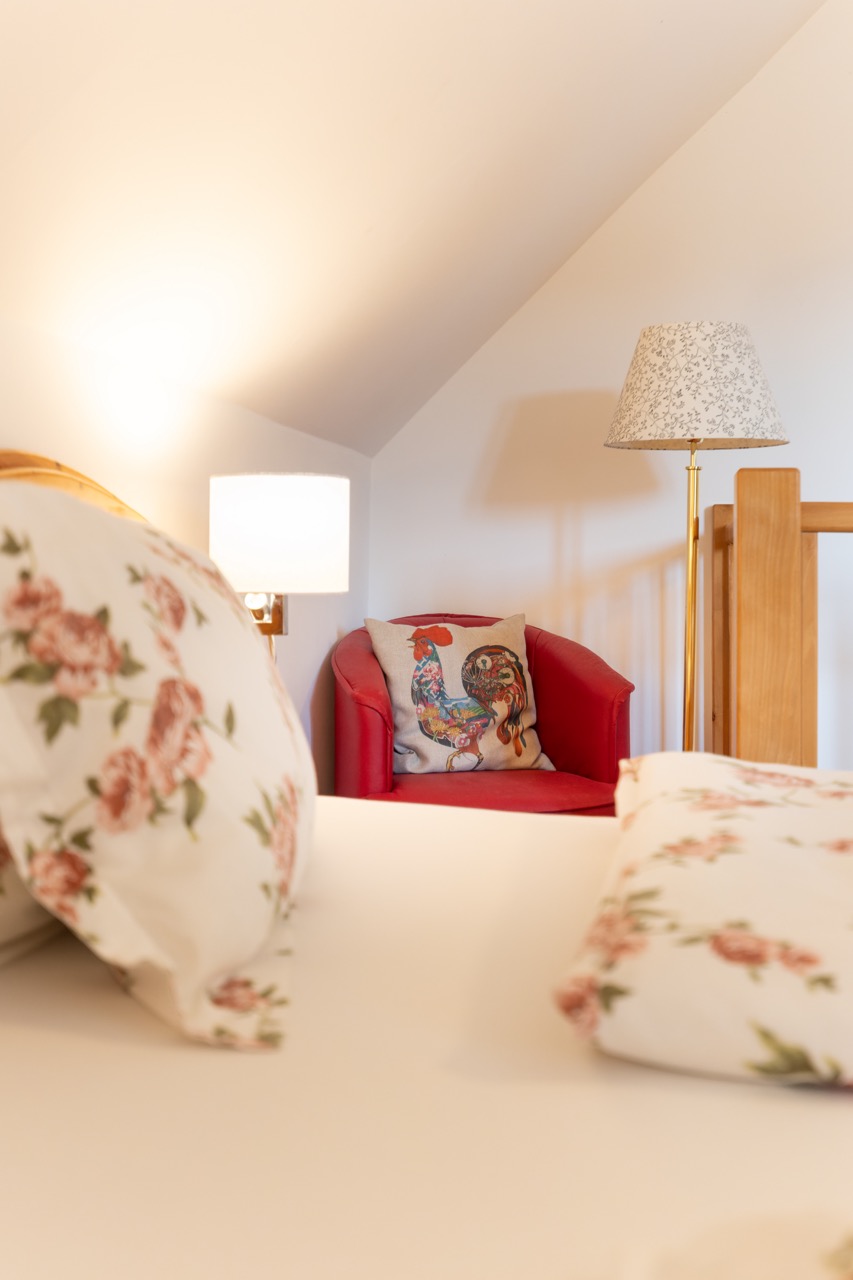 Neben dem Doppelbett stehen ein gemütlicher roter Stuhl und eine Leselampe.