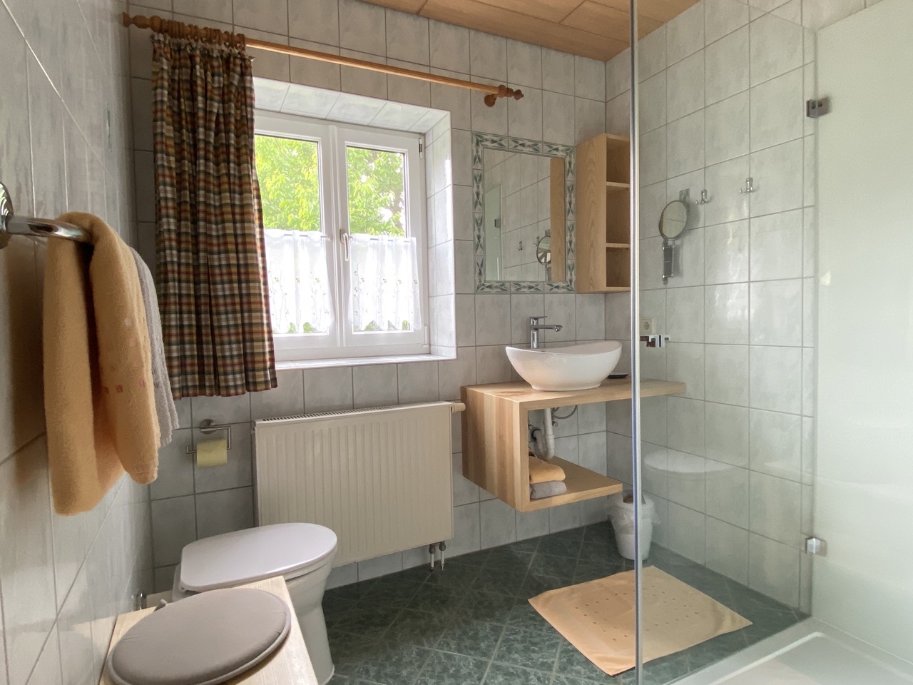 Wohnung mit großem, hellen Badezimmer und WC. Ein großes Fenster sorgt für schönes Tageslicht. Moderne Dusche und ansprechende Möblierung aus hellem Holz.