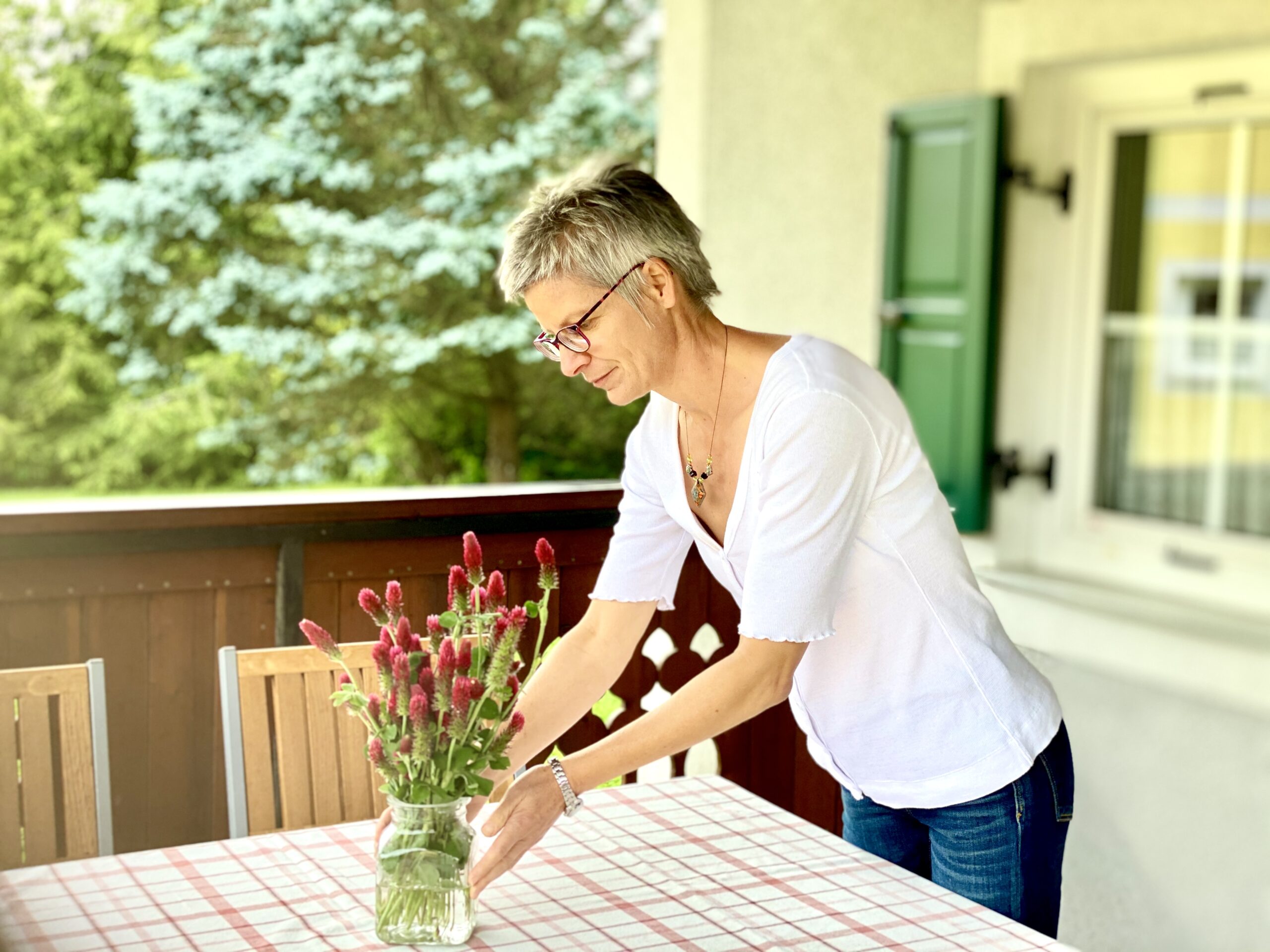 Ferienwohnung Terrasse Einladende Terrasse mit Holztisch, Stühlen und Blumen und Bäume im Hintergrund