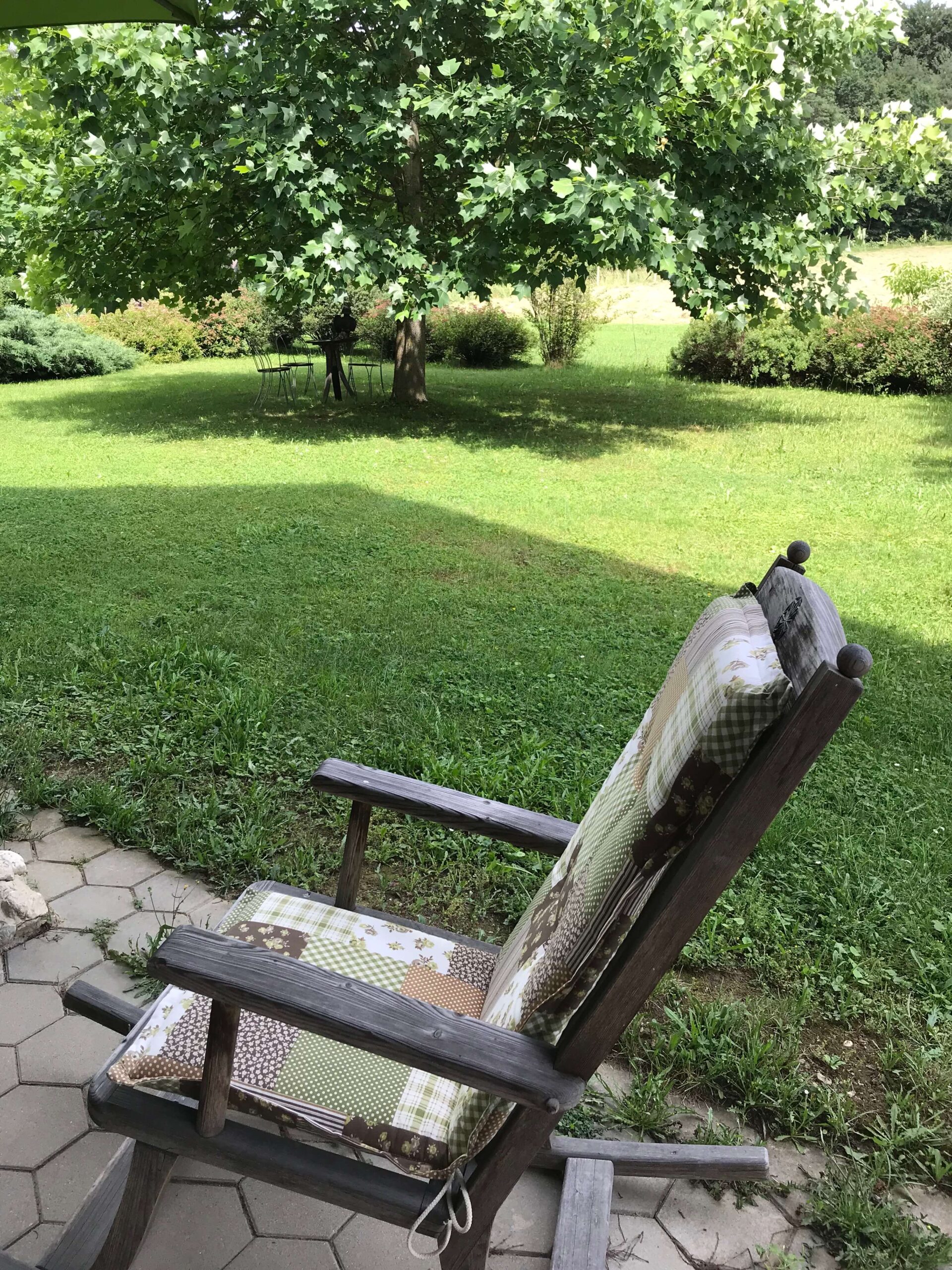 Holzschaukelstuhl auf der Terrasse mit direkten Gartenzugang. Schöner Baumbestand und Liegewiese.