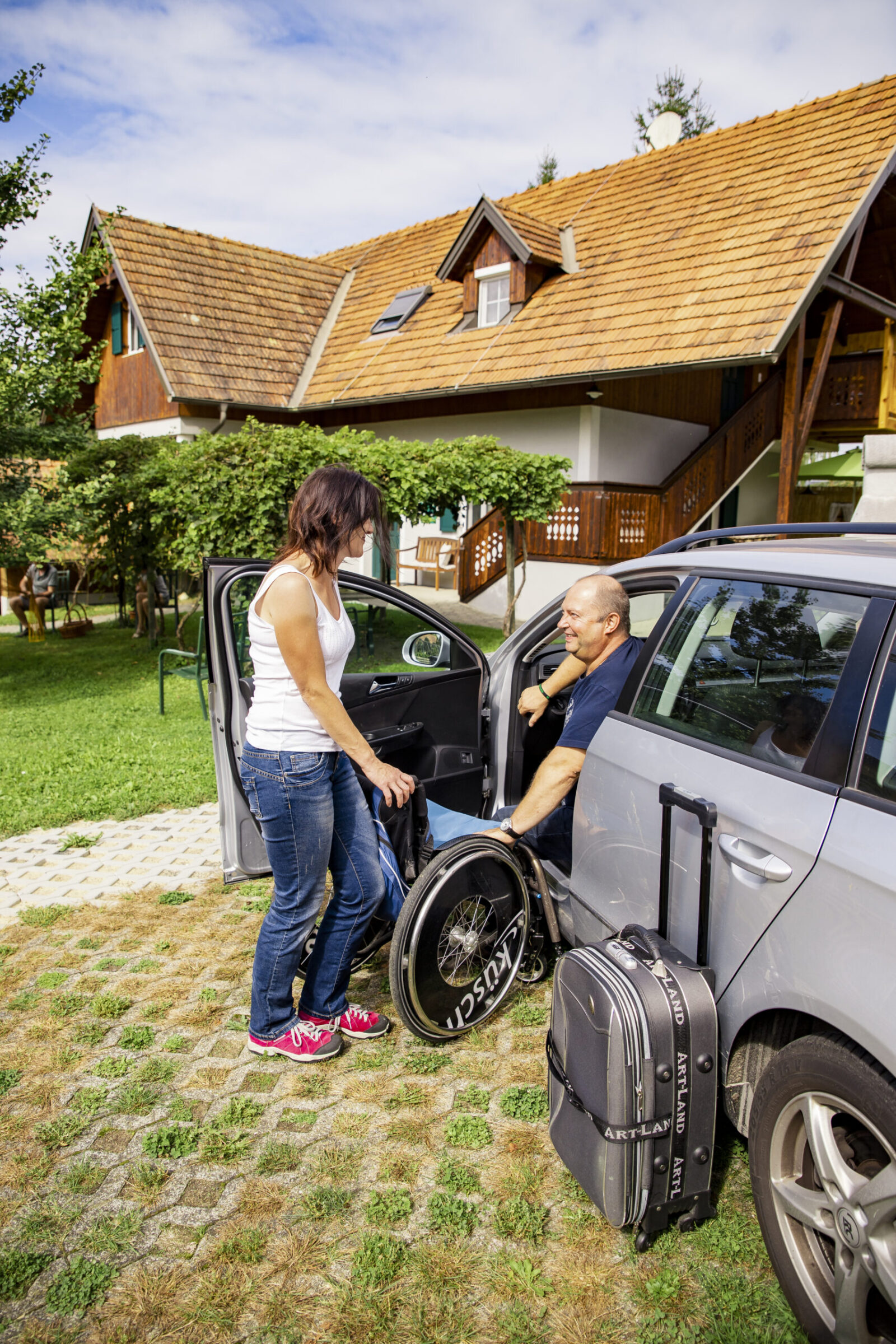 Ein Mann schaut aus dem Auto und eine Frau bringt ihm den Rollstuhl.